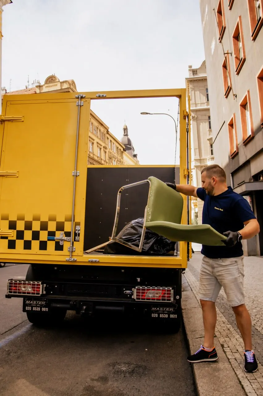 Řidič Odpad Taxi nakládá starou židli do žlutého vozu v centru Prahy